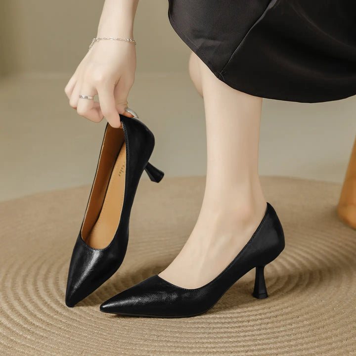 A pair of black faux leather pointed-toe pumps with a sculpted flared kitten heel, shown on a woman&