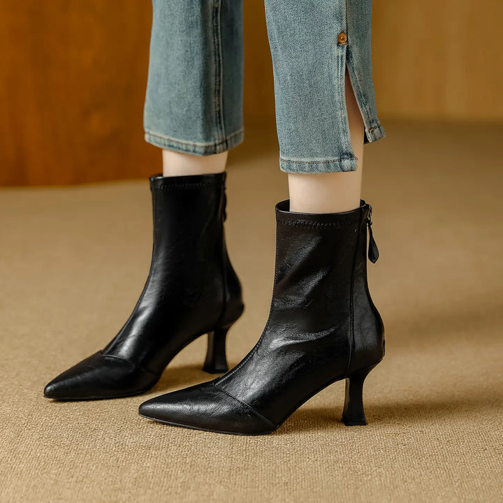 Black faux leather pointed toe ankle boots with a stiletto heel, worn by a model with cropped jeans featuring side slits.