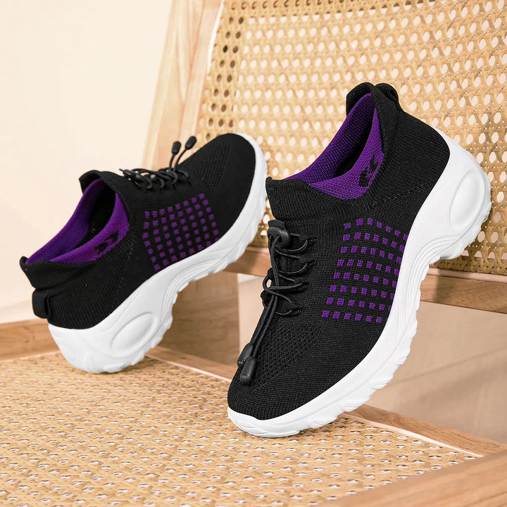A pair of black knit sneakers with a bright purple geometric square grid pattern, featuring purple lining, black quick-lace system, and thick white sculpted soles.