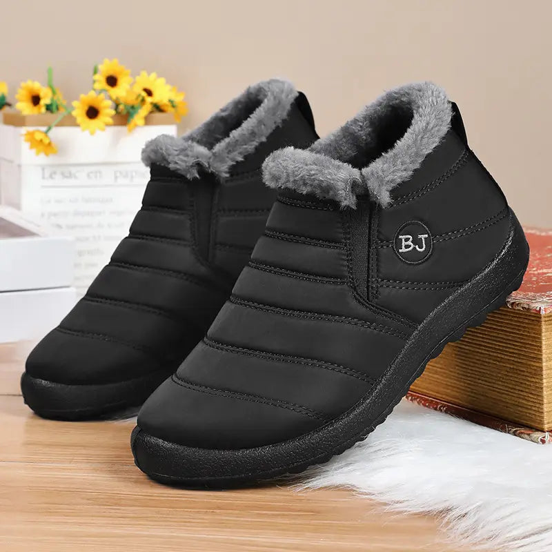 Faelan unisex black quilted nylon ankle boots with light grey faux fur lining and side elastic panels, featuring a circular 'BJ' logo detail and a flat rubber sole.