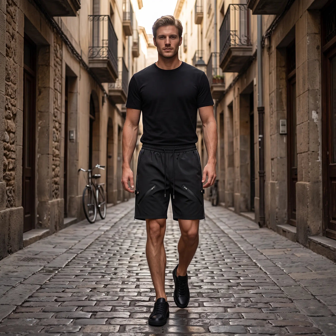 Matte black relaxed-fit technical shorts with diagonal zip pockets and rear snap button details. Features an elasticated waistband and clean hem.