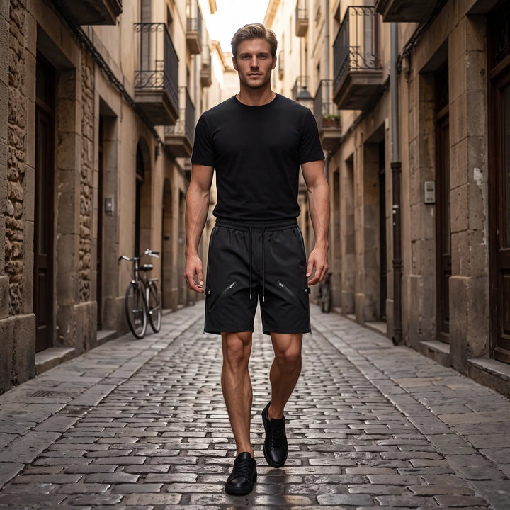 Matte black relaxed-fit technical shorts with diagonal zip pockets and rear snap button details. Features an elasticated waistband and clean hem.