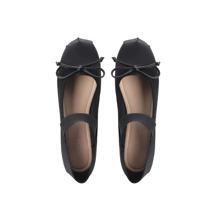 A pair of black satin ballet flats with a delicate bow on the vamp and a visible elastic instep strap, shown from a top-down view on a white background.