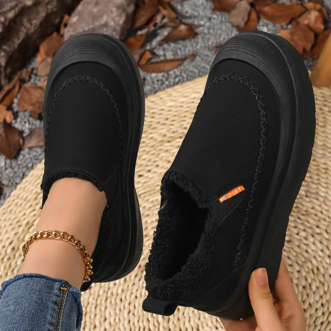 Black slip-on winter boots with plush shearling lining, detailed with contrast zig-zag stitching and a small orange &