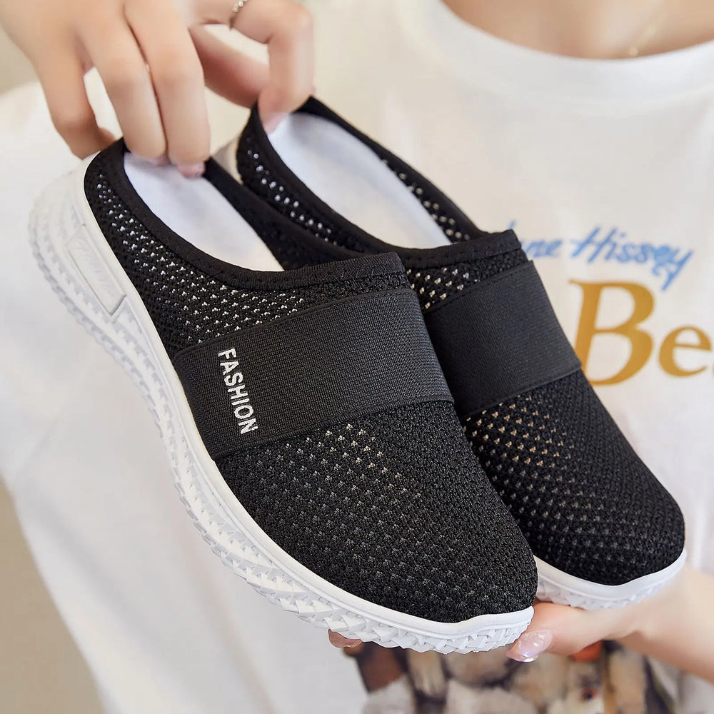 Pair of black women's slip-on mesh trainers with a white textured sole and elasticated instep strap featuring 'FASHION' text.