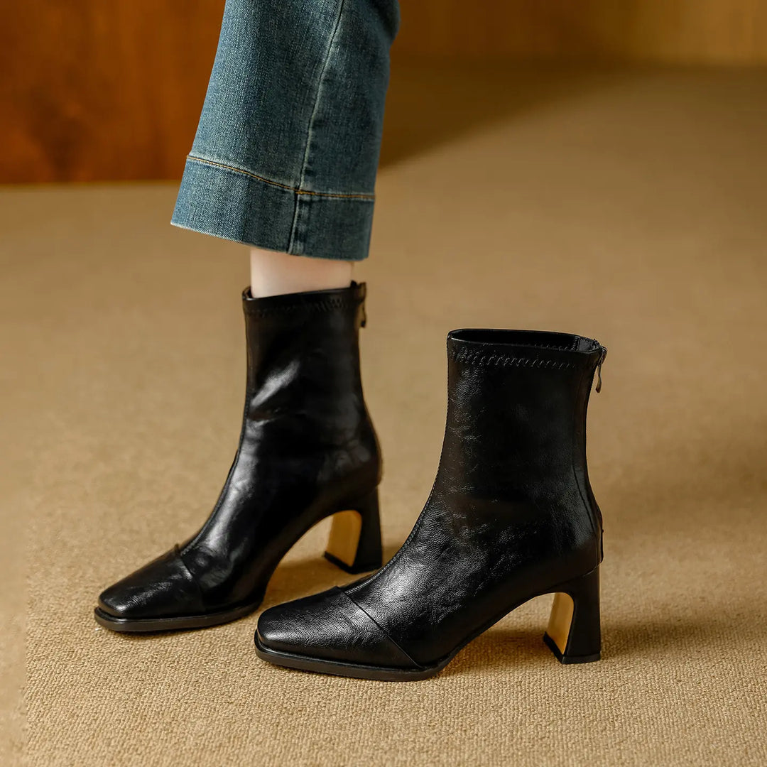 Chic black leather ankle boots with square toes and gold-finish block heels, worn with denim jeans for a stylish, everyday look.