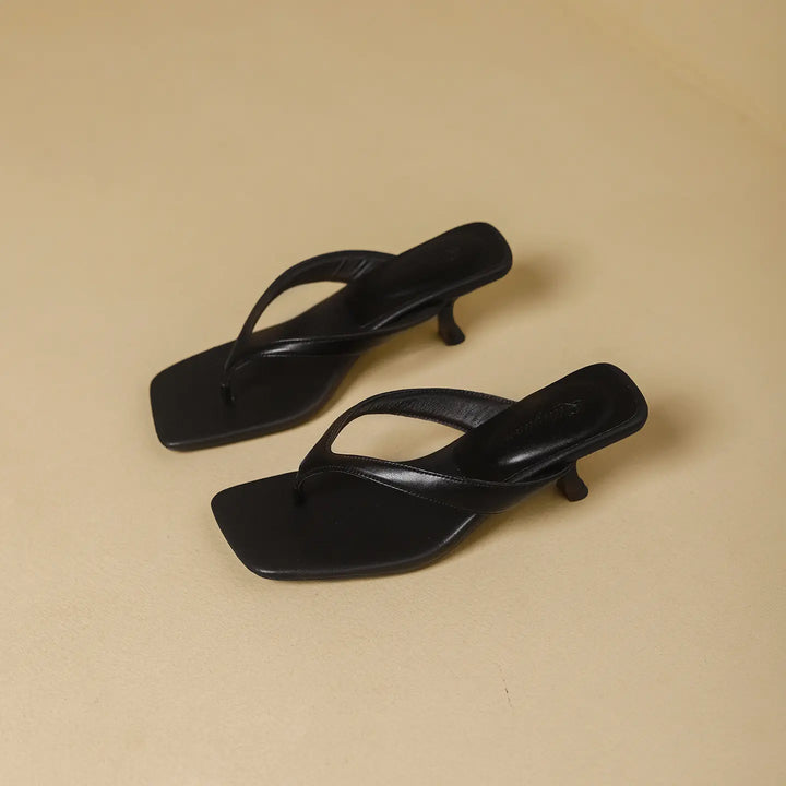 Pair of black heeled flip-flop sandals with a square toe and thin straps, showcased on a neutral studio background.