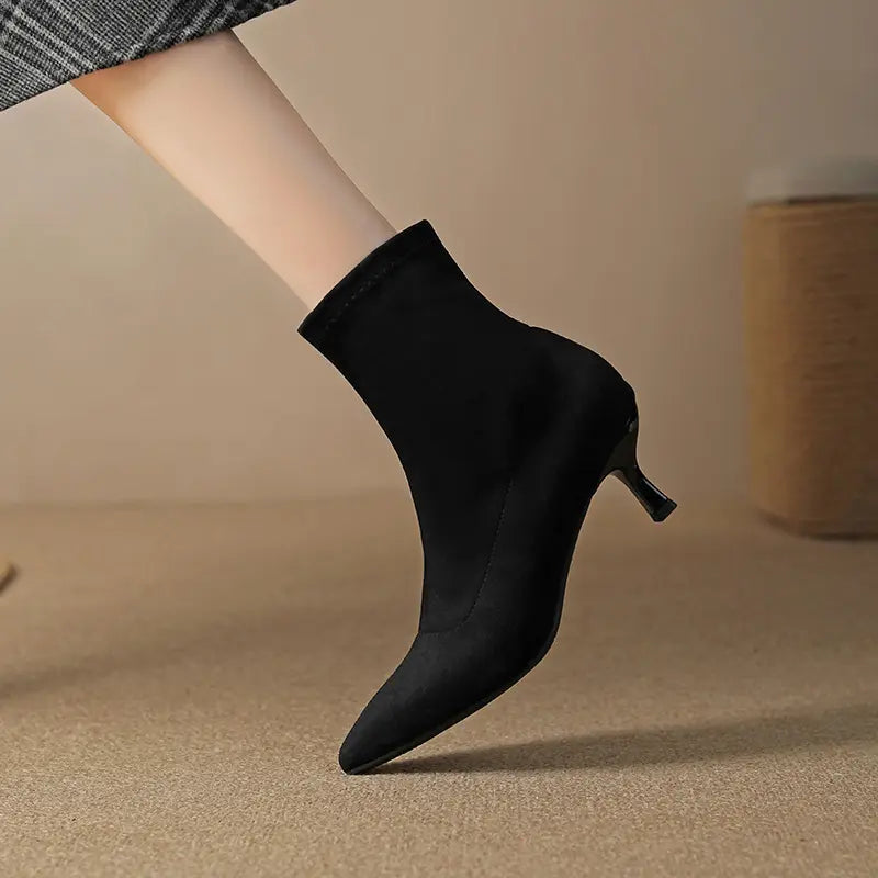Black suede-like stiletto ankle boot with a pointed toe and stretch sock-fit shaft, shown on a model&