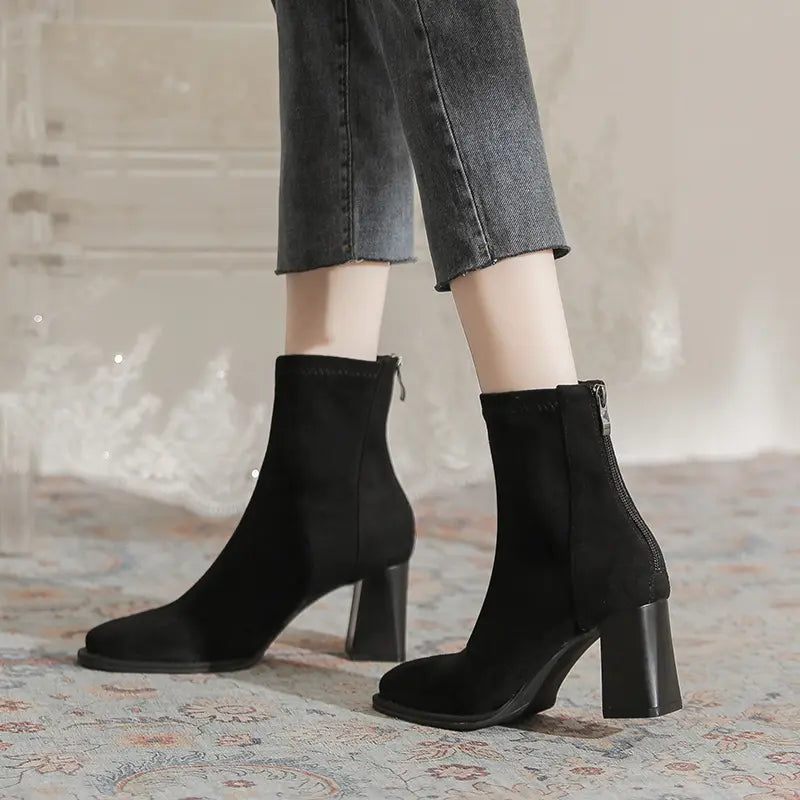 Black suede-like ankle boots with a square toe and chunky block heel, featuring a back zipper, shown worn with cropped jeans.
