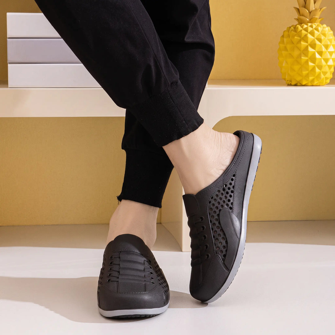 A pair of black ventilated mule clogs with a slip-on design and faux lace-up detail, shown on a person&