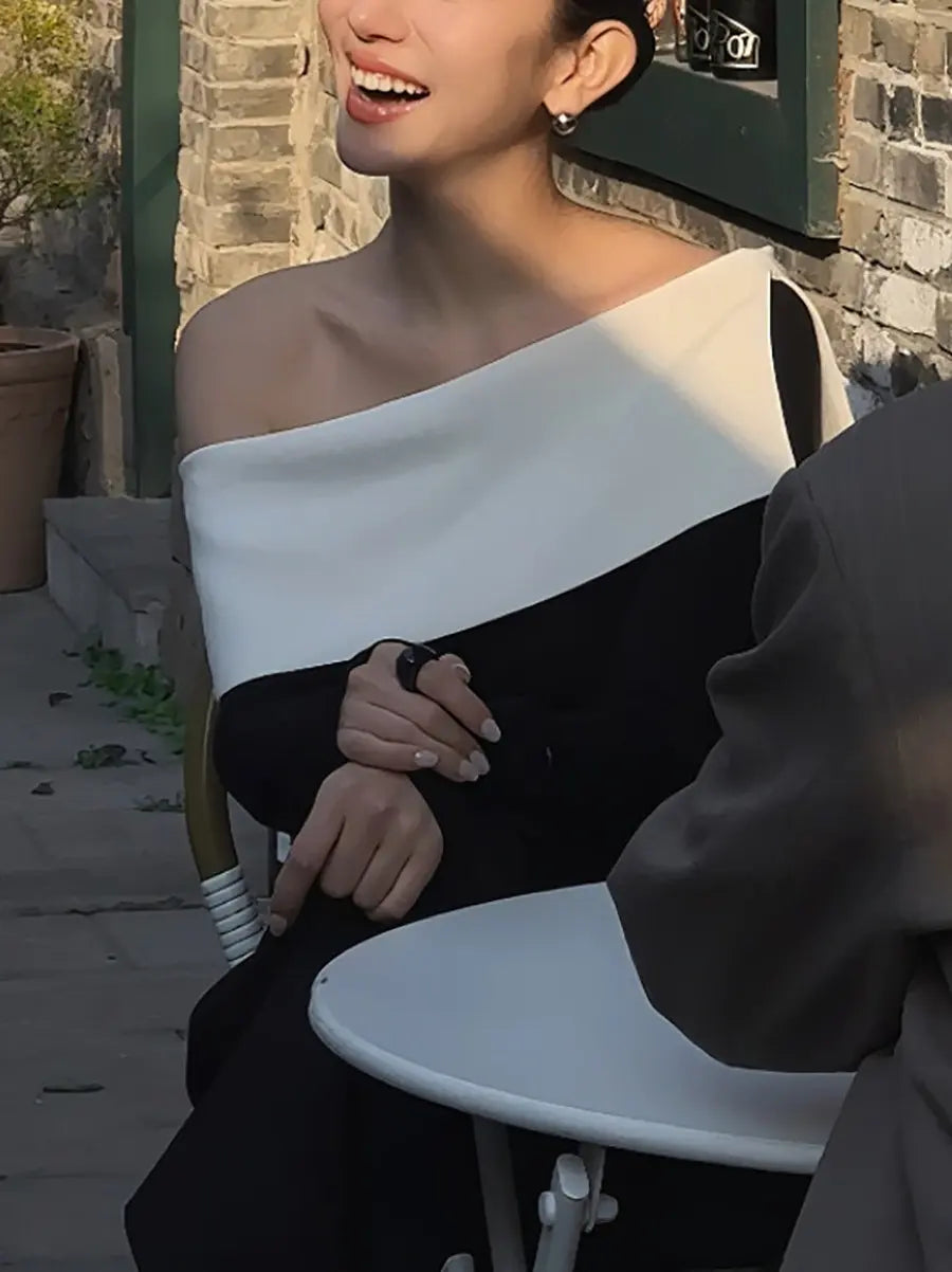 Woman wearing a chic black and optic white asymmetrical off-shoulder knit top in an outdoor lifestyle setting, showcasing modern elegance.