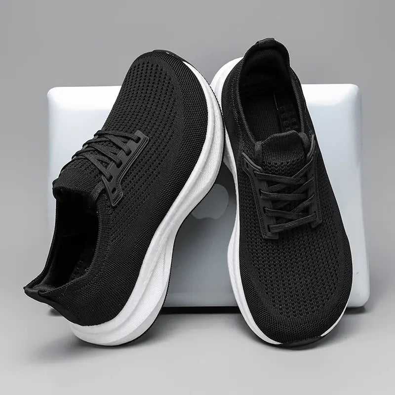 Black wide fit breathable athletic trainers with a chunky white EVA sole and black rubber outsole, presented from a three-quarter front view on a neutral grey studio background.