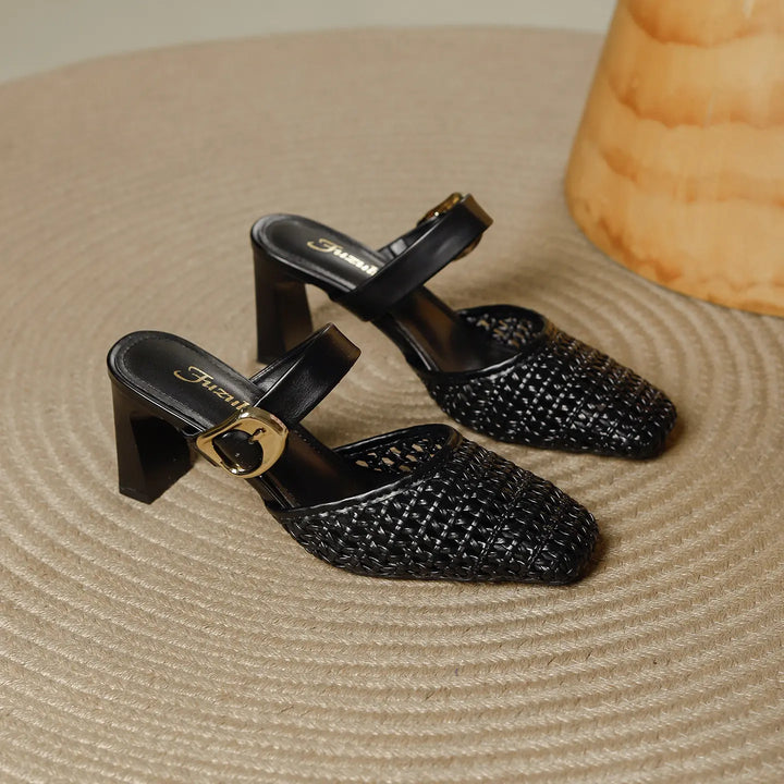 Black woven square-toe block heel mules featuring a slender ankle strap with a polished gold-tone buckle, presented on a textured surface.