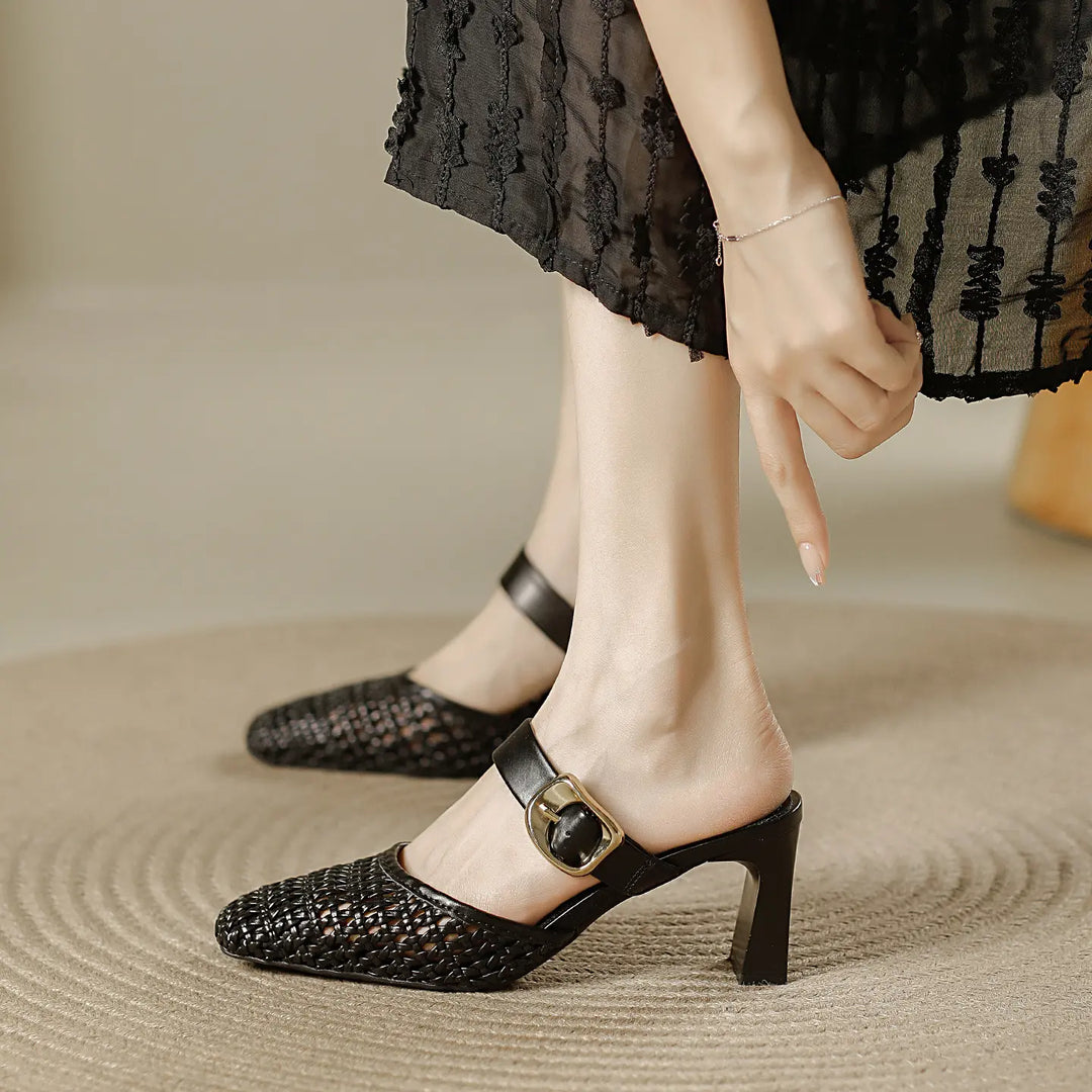 Black woven square-toe block heel mules with a gold buckle and adjustable ankle strap, shown on a model&