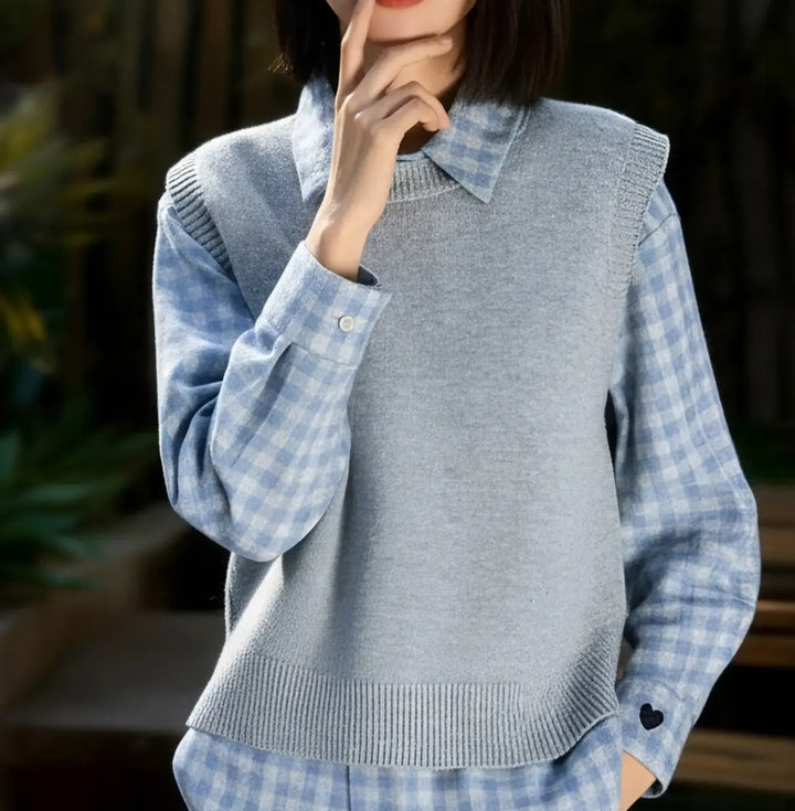 A woman models a stylish layered outfit featuring a blue plaid collared shirt paired with a light grey knitted vest, showcasing a relaxed and chic casual look.