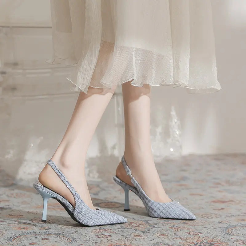 Model wearing chic light blue woven tweed-like slingback heels with a pointed toe and stiletto heel, paired with a flowing dress.