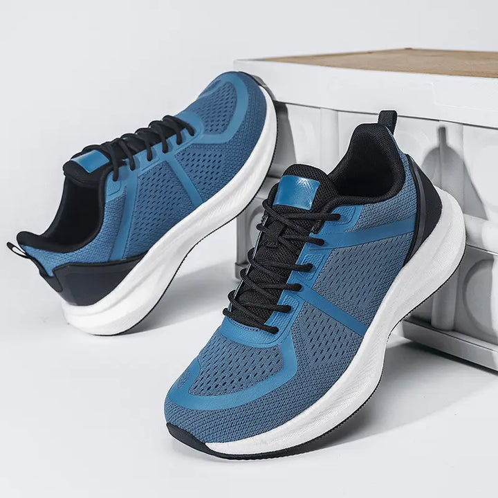 Pair of blue wide-fit breathable athletic trainers shown from a three-quarter side view, featuring a mesh upper, white EVA midsole, and black rubber outsole.