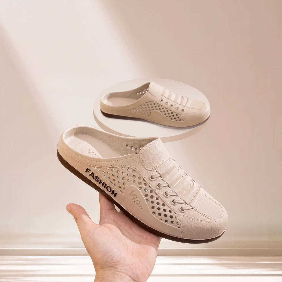 Pair of light beige breathable clogs with perforated detailing and faux lace-up design, shown with one shoe held by a hand. Features &