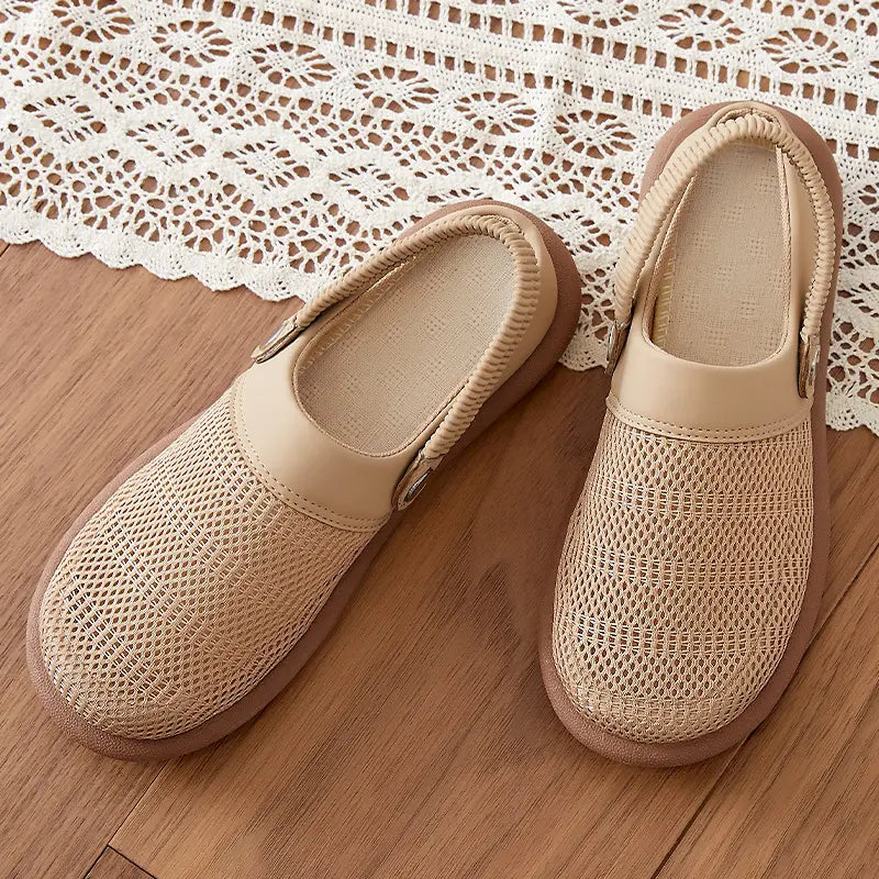 Pair of beige breathable mesh slip-on mules with synthetic trim and an elasticated heel strap, displayed on a wooden surface with a decorative lace overlay.