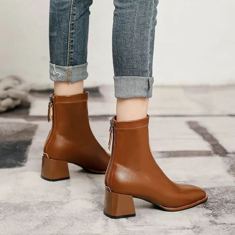 Brown faux leather ankle boots featuring a chic square toe, a stable block heel, and a functional rear zipper, paired with cuffed denim jeans.