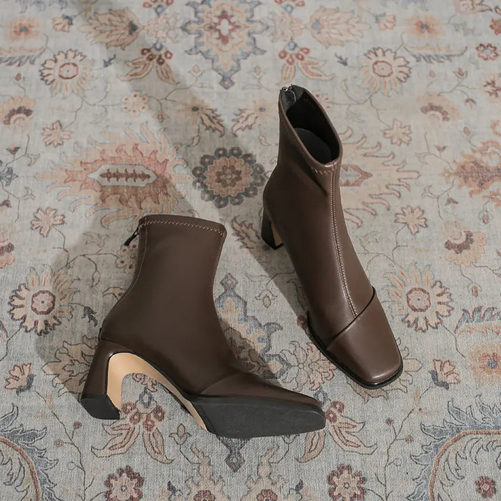 Riven brown faux leather ankle boots with a square toe and block heel, shown from a three-quarter angle on a patterned rug.