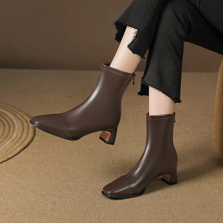 Brown faux leather square toe ankle boots with block heels, worn with black cropped trousers in a lifestyle setting.