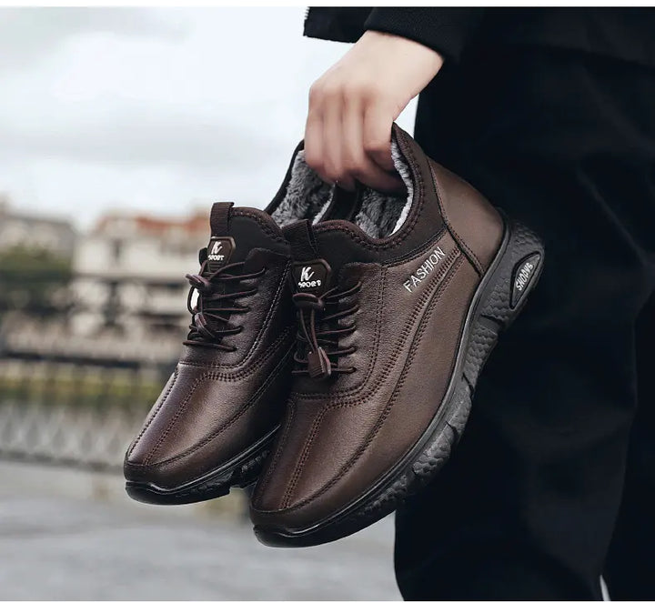 A pair of brown PU leather lace-up winter boots with faux fur lining, held by a person with a blurred outdoor background. Features white embroidered &