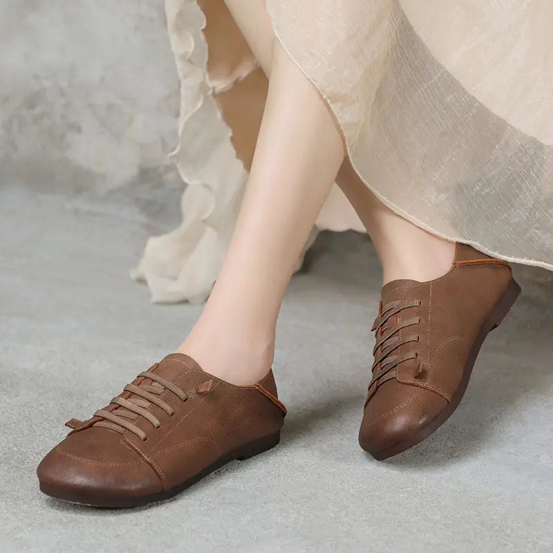 Brown leather retro comfortable sneakers worn by feet, showcasing supple matte texture, round toe, and decorative flat laces on a neutral background.