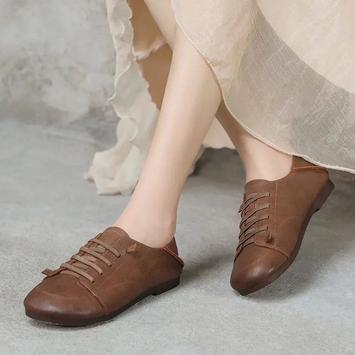 Brown leather retro comfortable sneakers worn by feet, showcasing supple matte texture, round toe, and decorative flat laces on a neutral background.
