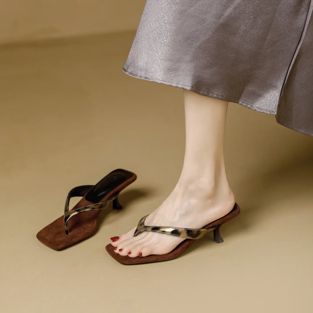 A woman's foot wearing a brown heeled flip-flop sandal with a leopard print accent strap and square toe, next to a matching sandal on a studio background.