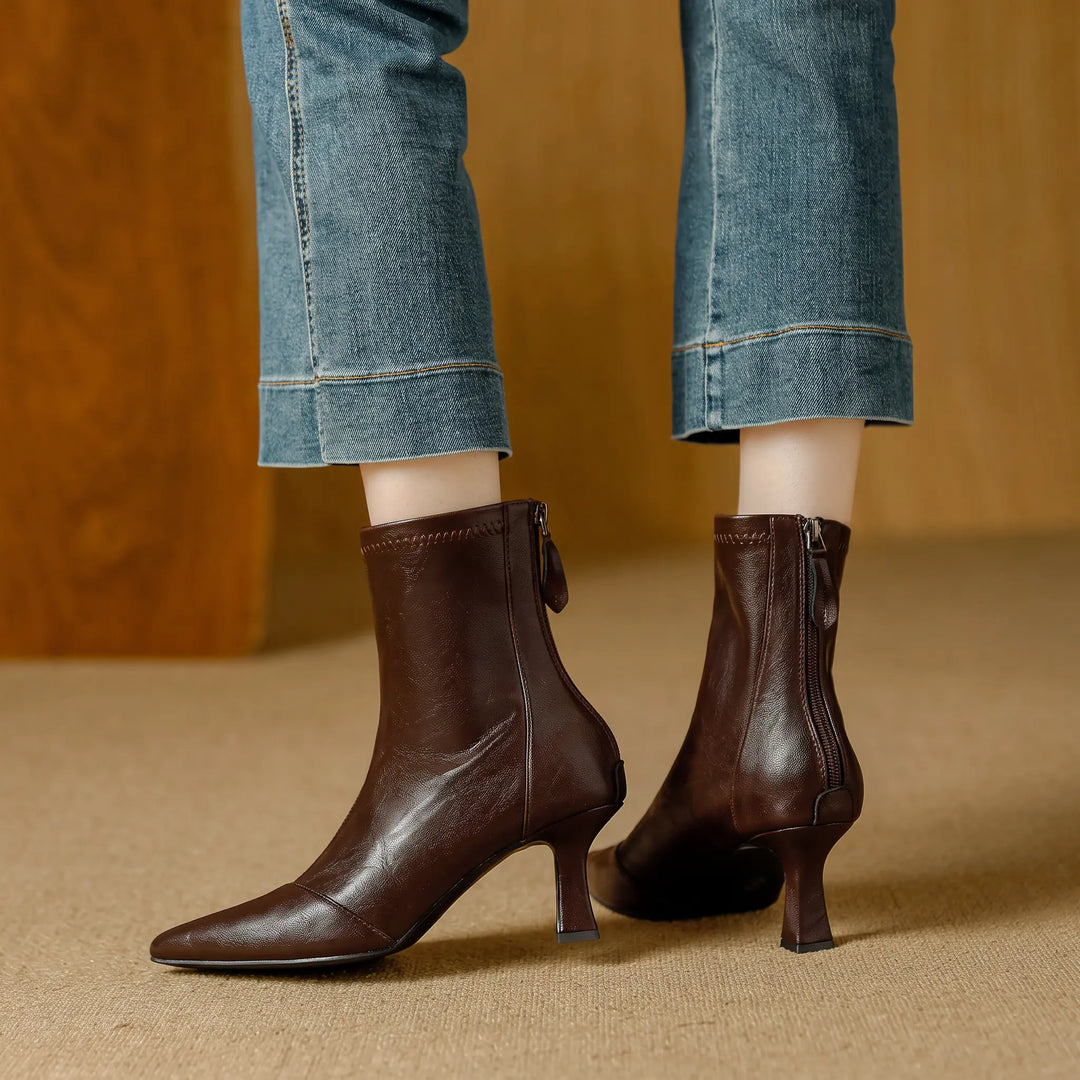 Brown faux leather ankle boots with a pointed toe and stiletto heel, featuring a back zipper closure, styled with cropped denim jeans.