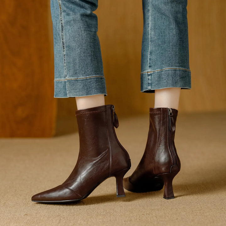 Brown faux leather ankle boots with a pointed toe and stiletto heel, featuring a back zipper closure, styled with cropped denim jeans.