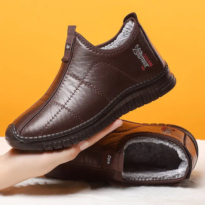 Brown quilted synthetic leather slip-on winter boots lined with fluffy grey faux fur, shown in a three-quarter view with a subtle embroidered emblem on the side.