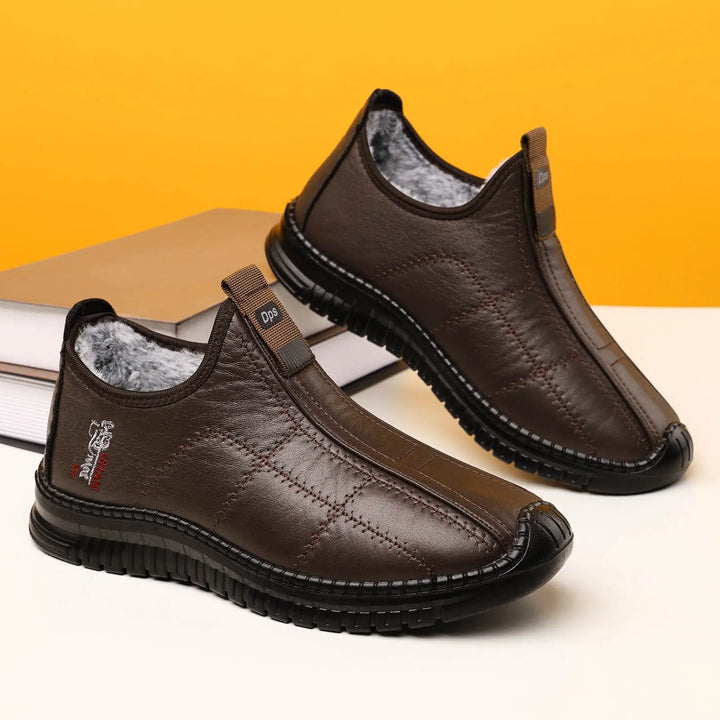 Brown quilted synthetic leather slip-on winter boots lined with fluffy faux fur, shown at a three-quarter angle on a studio backdrop with books.