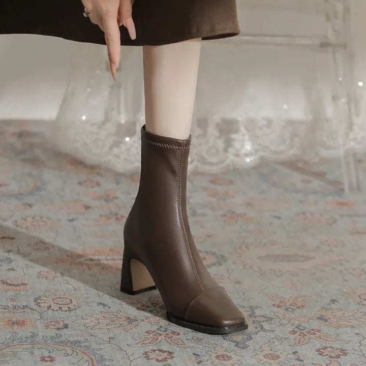 Brown faux leather square toe ankle boot with a block heel and mid-calf shaft, shown on a leg with a decorative rug background.