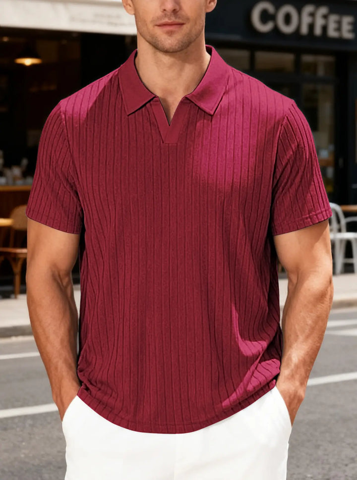 Man wearing a burgundy textured knit polo shirt with fine vertical ribs and a deep V-neck collar, styled casually with white pants in an outdoor setting.