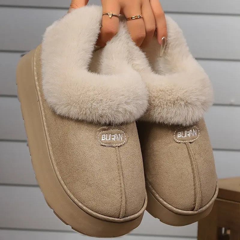 Warm camel suede-like mule slippers with plush faux fur lining and an embroidered BUAN logo, shown held up from a three-quarter angle.