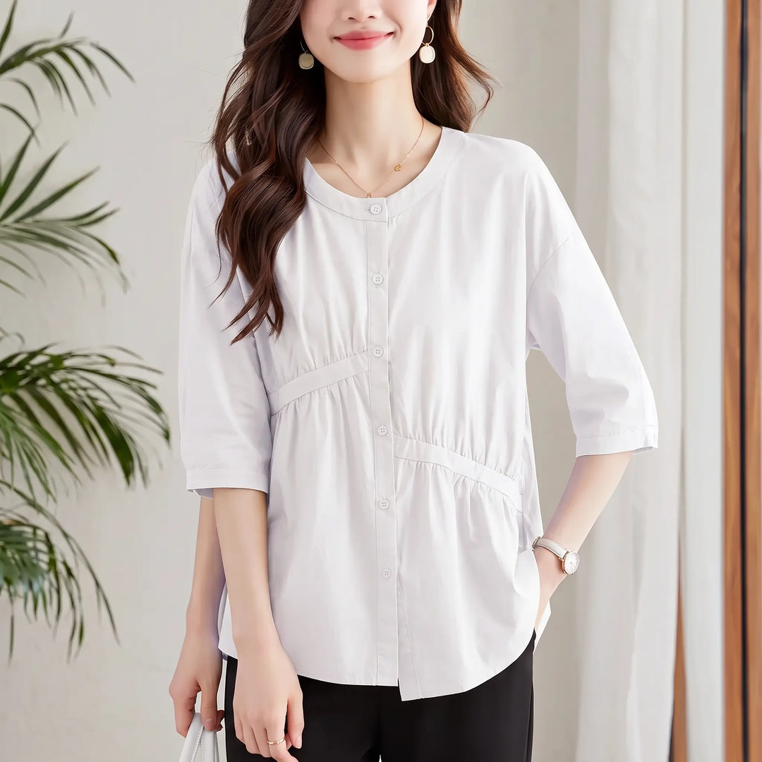 Chic white cotton blouse featuring an asymmetric peplum hem, diagonal waist pleating, a round neckline, and 7/8 sleeves with button cuffs.