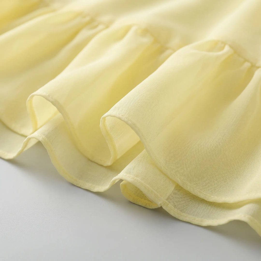 Close-up of pale yellow chiffon midi dress fabric showcasing delicate cascading ruffles and sheer texture. Detailed view of the romantic tiered hem and flowing material.