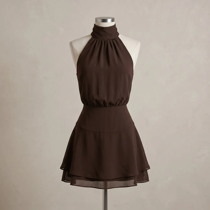 Chocolate brown halter neck mini dress featuring a pleated blouson bodice, wide tailored waistband, and a subtly layered A-line skirt, presented on a mannequin.
