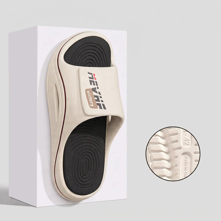 Chunky off-white EVA slide sandal with a black textured footbed and a single wide strap featuring the MEVRHE VICTORY logo. The sculpted sole has curved lines and a side cut-out detail.