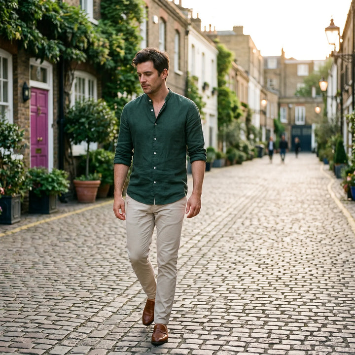 A man walks down a cobblestone street wearing a dark green mandarin collar linen blend shirt and beige chinos, showcasing a sophisticated casual urban style.