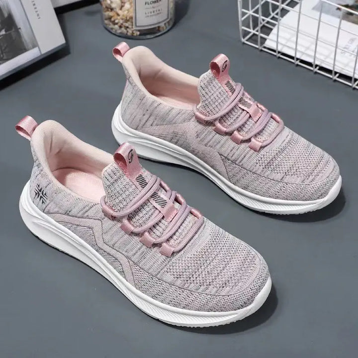 Dusty rose and grey knit athletic trainers for women, featuring a breathable mesh upper, wavy side detail, flat pink laces, and a sculpted white sole. These comfortable, stylish sneakers offer a three-quarter view.