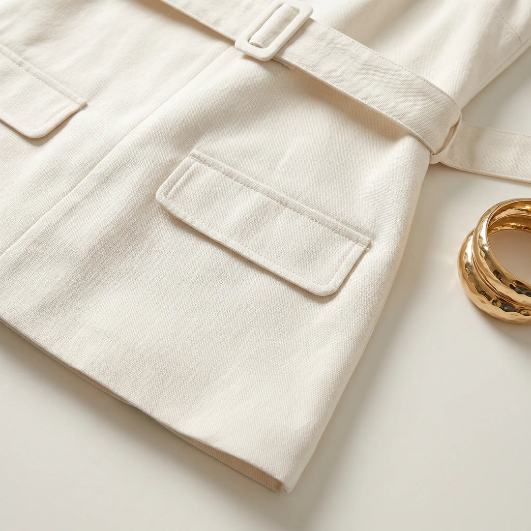 Close-up detail of a soft ecru linen-blend ensemble, showcasing a flap pocket, textured fabric, and belt buckle. Perfect for showcasing refined craftsmanship.