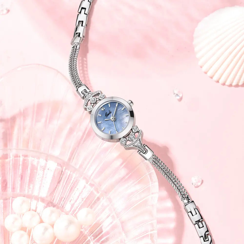 Elegant silver-tone bracelet watch with a delicate blue mother-of-pearl dial, crystal accents on the lugs, and a woven mesh strap.