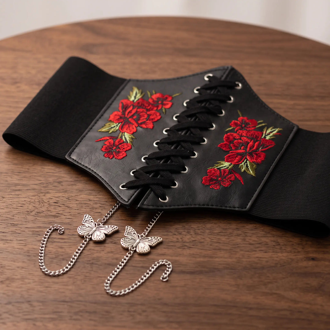 Wide black faux leather corset belt with vibrant red floral embroidery, black lace-up front, silver chains and delicate butterfly charms.