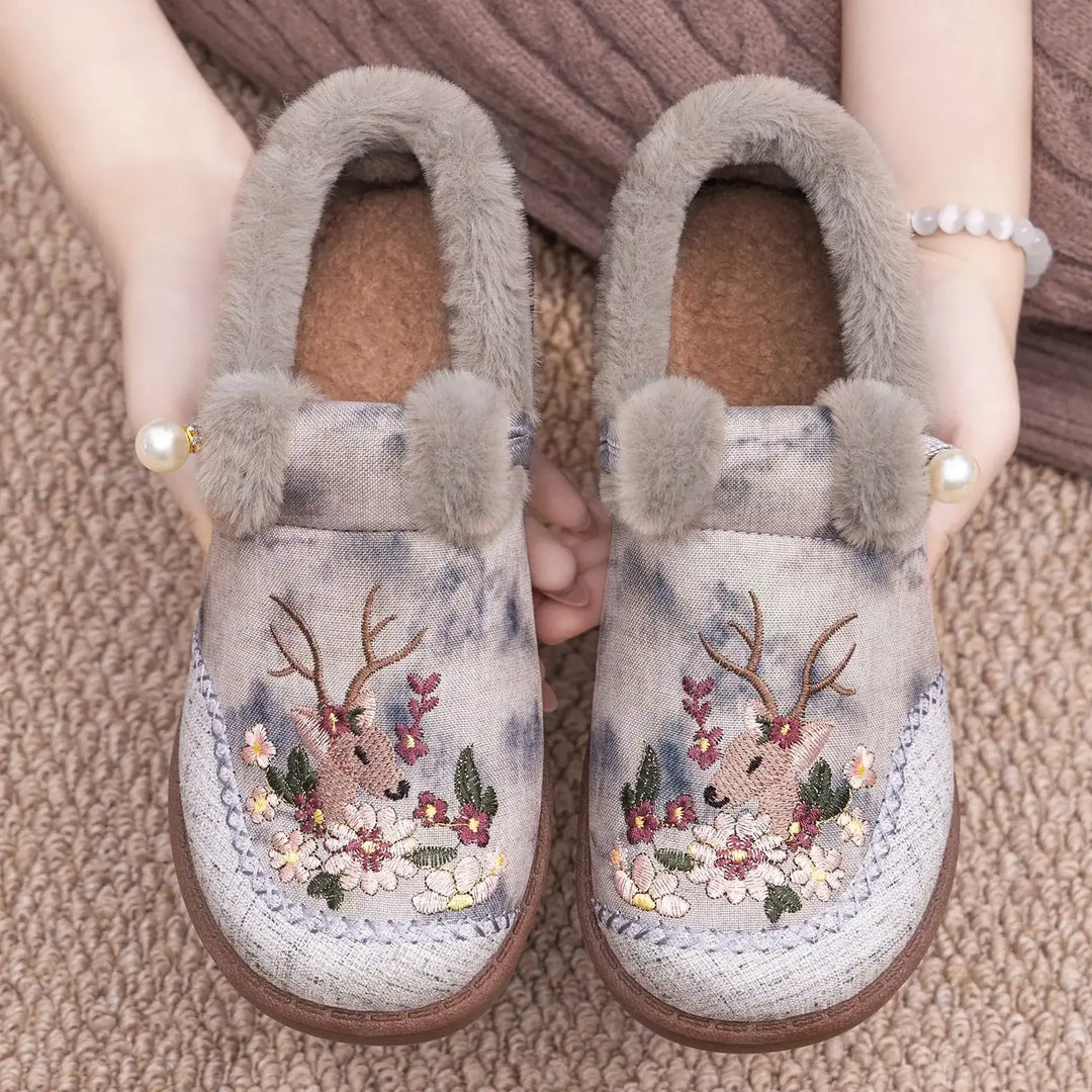 Embroidered plush slippers in dusty rose with muted watercolor print, featuring deer and floral motifs, grey faux fur trim, and a pearl accent.