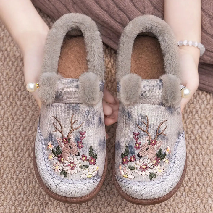 Embroidered plush slippers in dusty rose with muted watercolor print, featuring deer and floral motifs, grey faux fur trim, and a pearl accent.