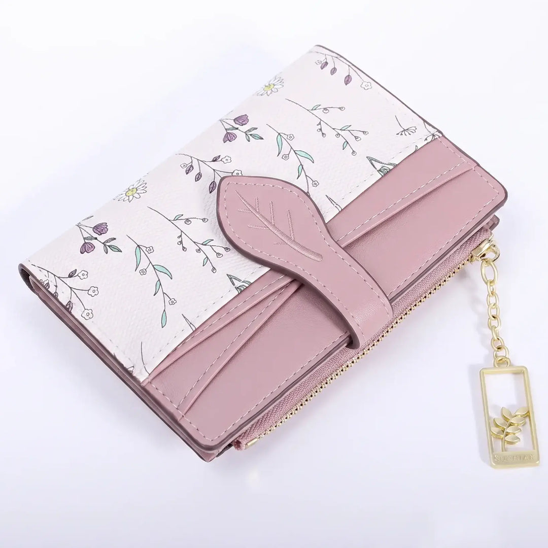 Dusty rose bi-fold wallet with a delicate off-white floral print, featuring a leaf-shaped tab closure and a gold-tone charm.