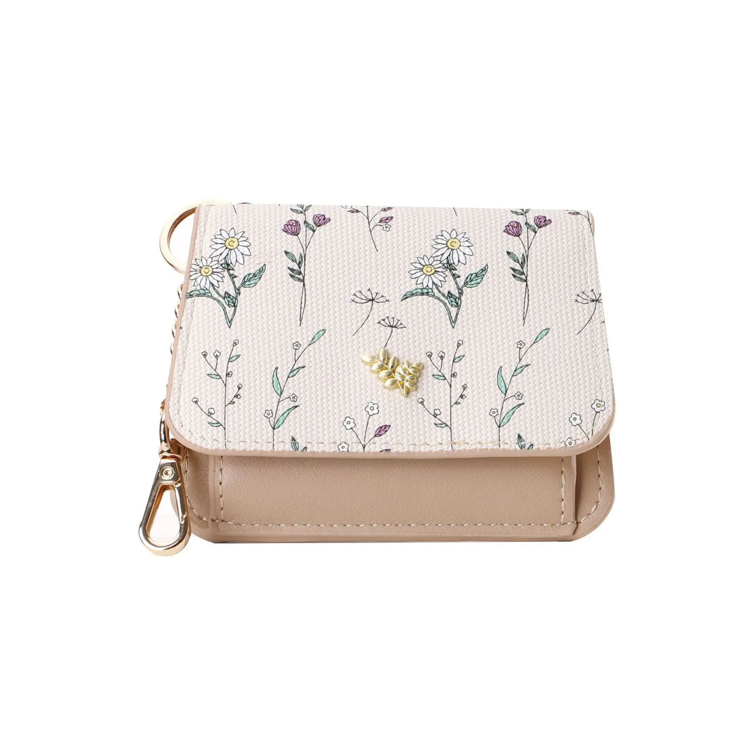 Compact tri-fold floral print PU leather wallet with snap closure and gold hardware, featuring a delicate daisy and wildflower pattern. A secure zippered compartment is on the back.